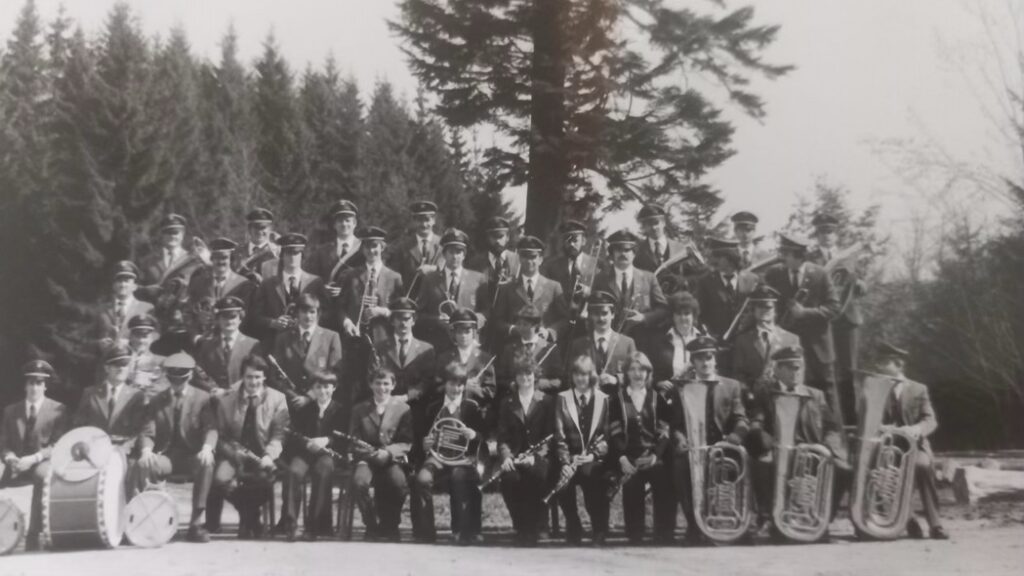 Es zeigt die Musikkapelle Mundelfingen und stammt aus dem Jahre 1983. Was sehen wir im Hintergrund? Die  Kohlwaldtanne und das Holzlager. Grund der Aufnahme sei kein Jubiläum gewesen, sondern das Schützenfest „Preussisch Oldenburg“ bei Minden. 