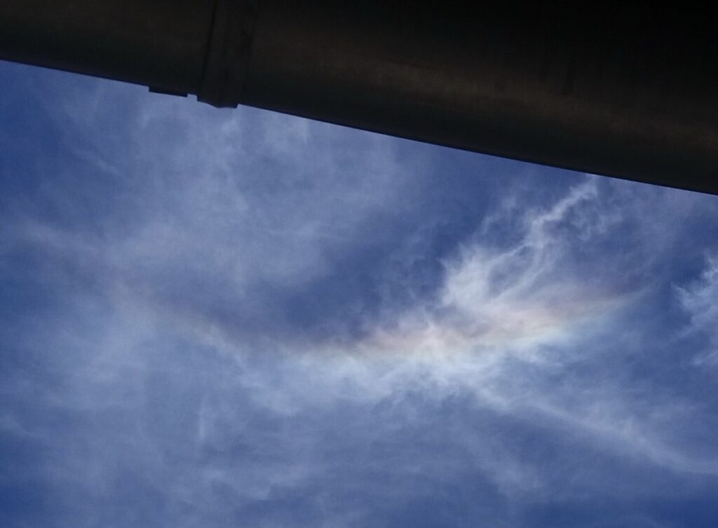Bild vom Himmel der überwiegend blau ist farbigem Bogen und Wolken