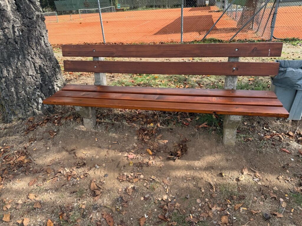 Bank auf dem zum Fussballplatz hin gerichter dahinter sieht man den Tennisplatz. Vor der Bank liegen viele Kippen